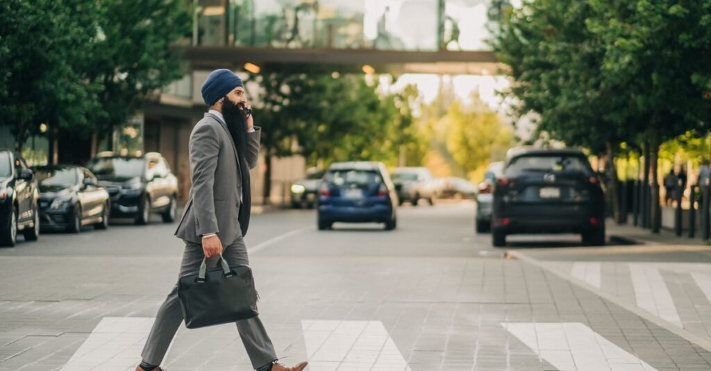 Sikh businessman with a turban crossing a city street on a zebra crossing, carrying a briefcase.